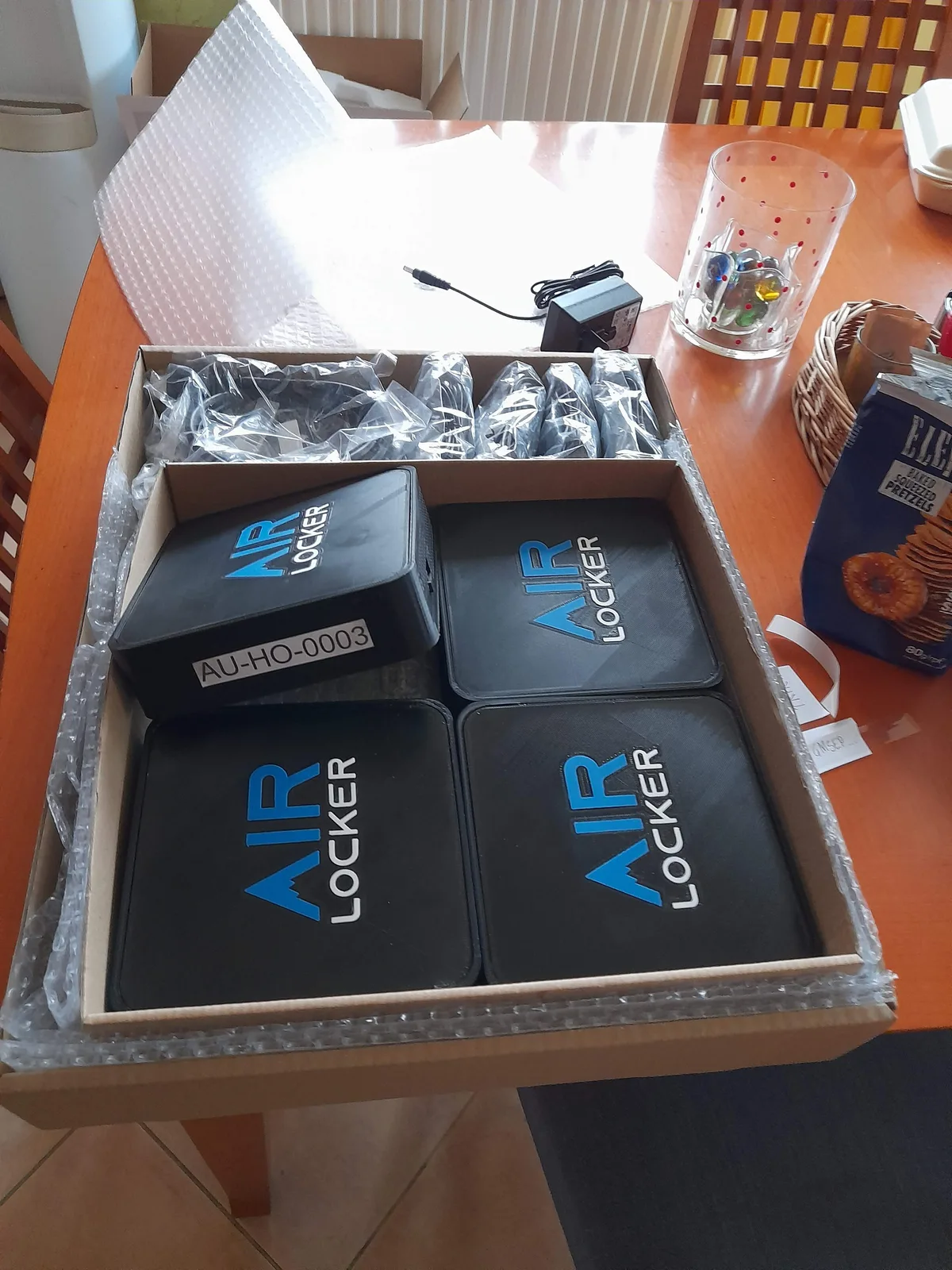 Five AIR LOCKER units packed into a cardboard box on a kitchen table, one carrying a printed asset label reading AU-HO-0003