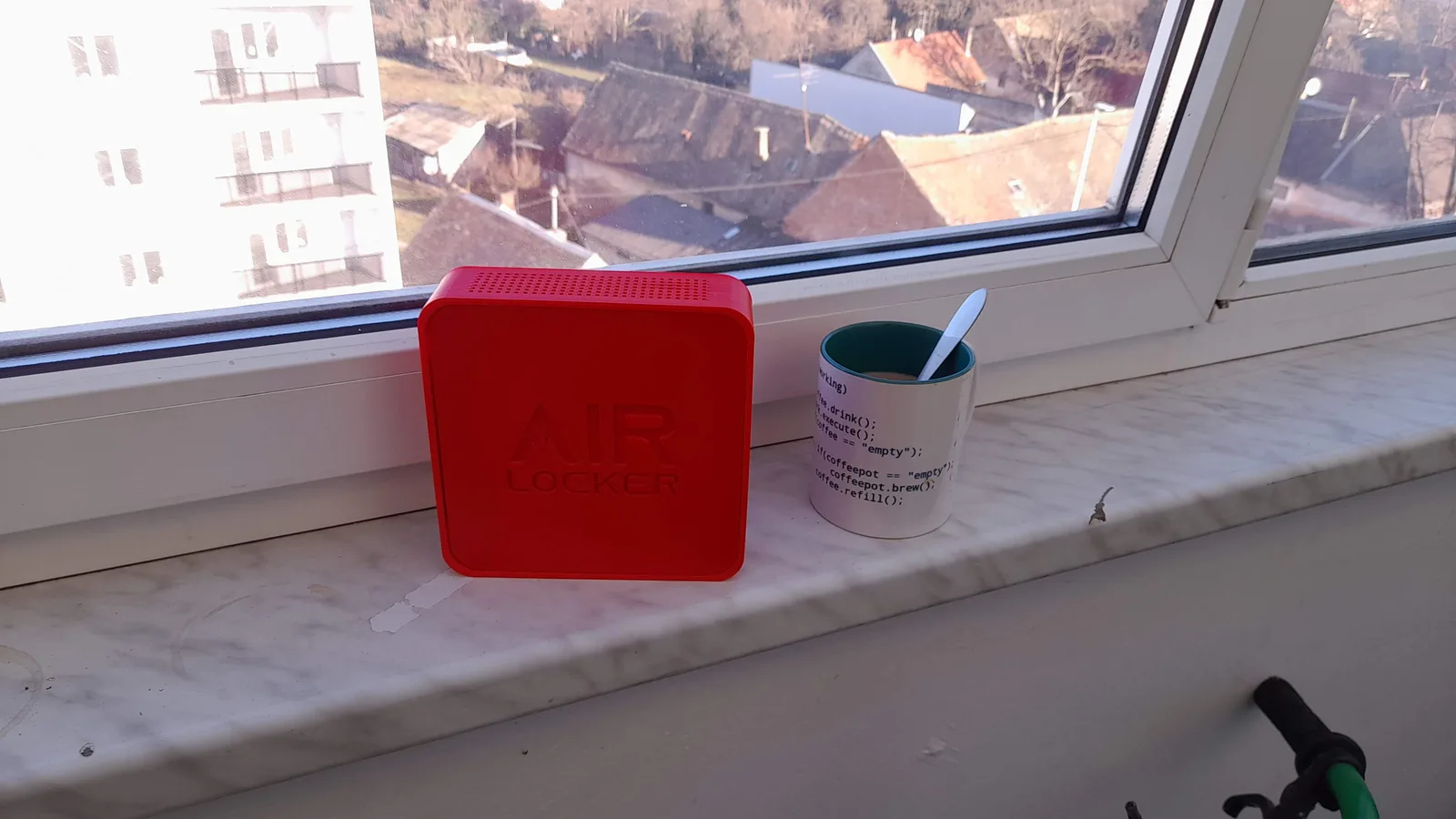 The first red 3D printed AIR LOCKER enclosure sitting on a windowsill with Croatian rooftops visible outside