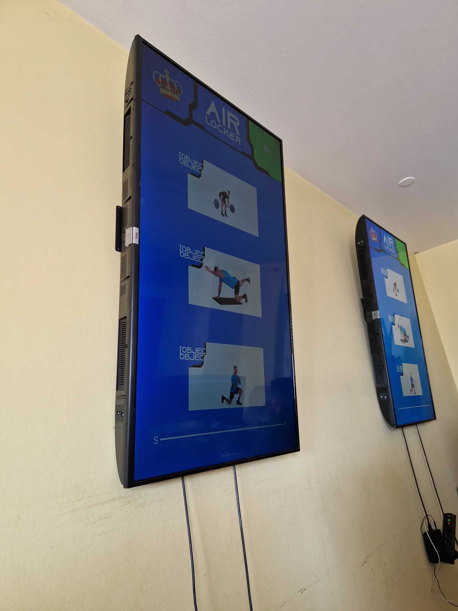 Two wall-mounted panels running the workout interface in portrait, showing stacked movement clips and a progress bar